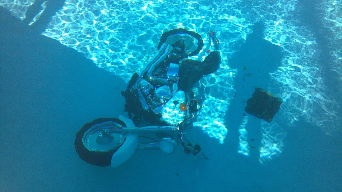 A person is riding a motorcycle underwater in a swimming pool.