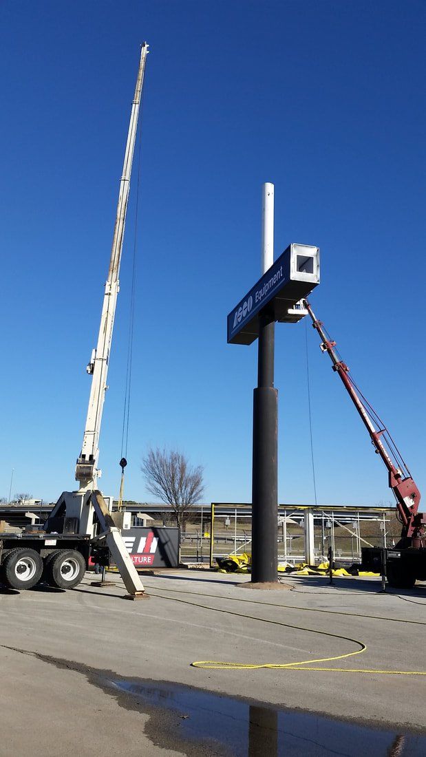A crane is lifting a large sign in a parking lot.