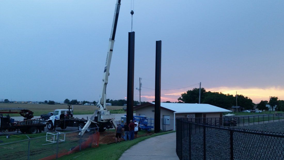 A crane is lifting a pole in a field.