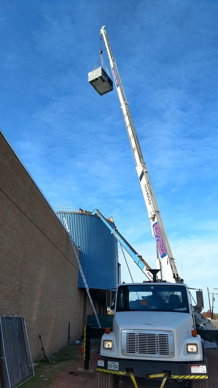 A white truck with a crane attached to it is parked in front of a building.