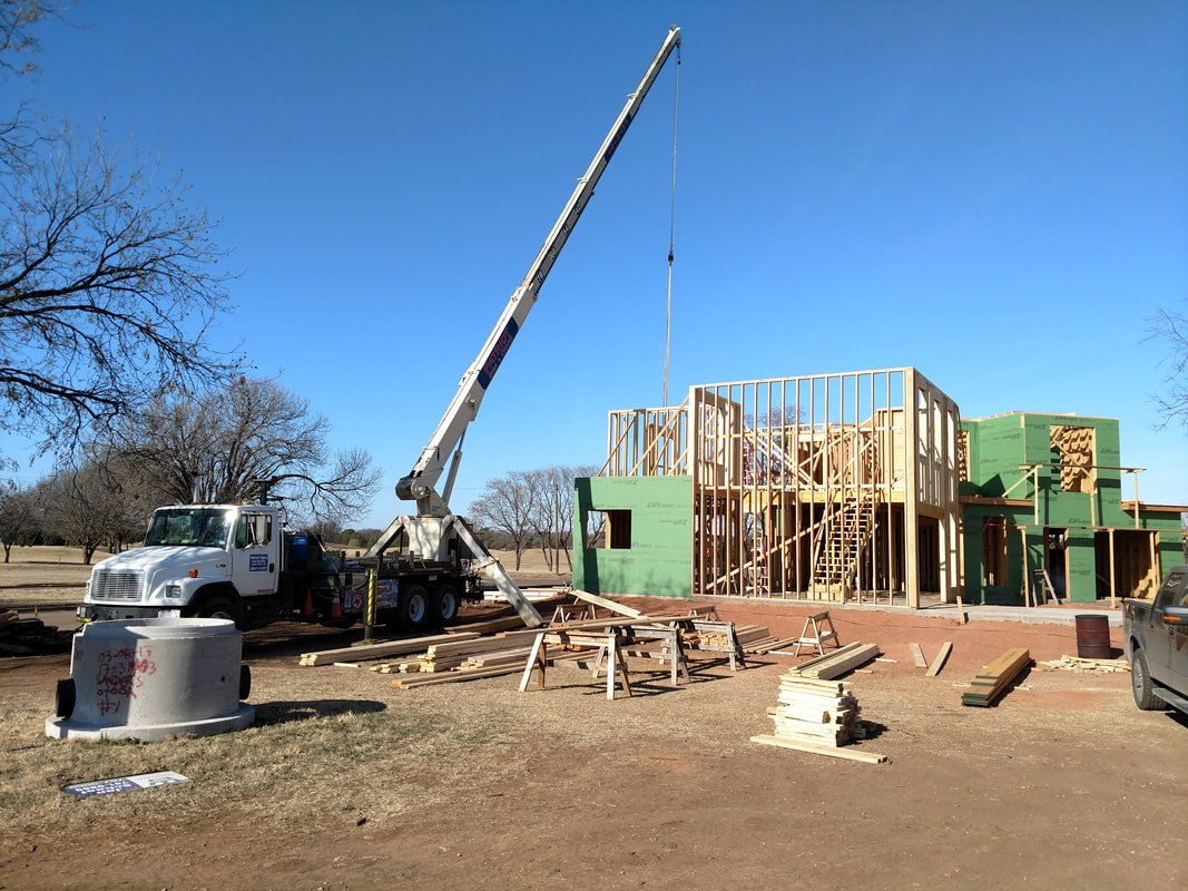 A crane is lifting a piece of wood in front of a house under construction.
