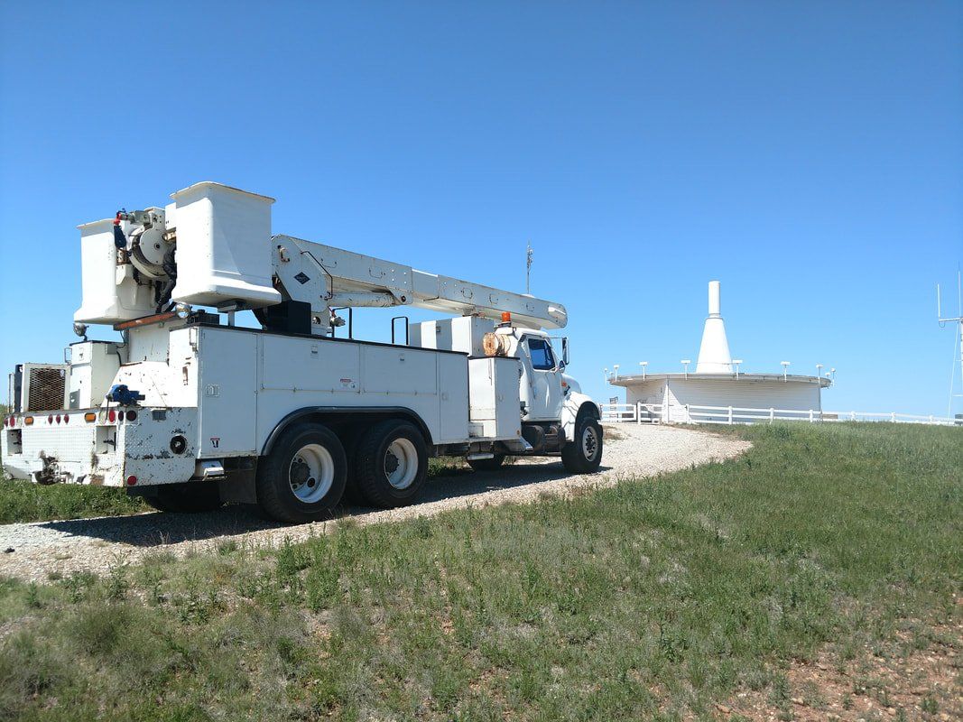 A white truck with a crane on the back is parked on a dirt road.