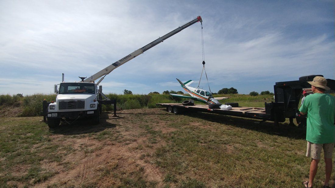 A crane is lifting a plane on a trailer in a field.
