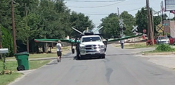 A truck is driving down a street with a plane on top of it.