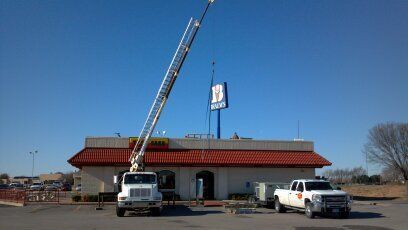 Two trucks are parked in front of a building with a ladder on top of it.