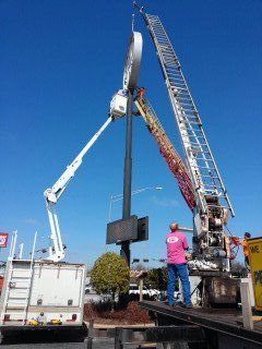 A man in a pink shirt is standing on a tow truck next to a crane.