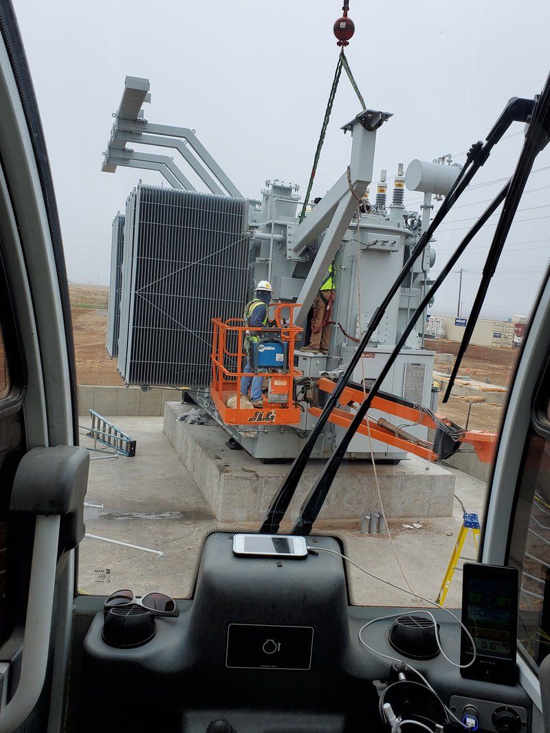 A crane is lifting a large transformer on a construction site.