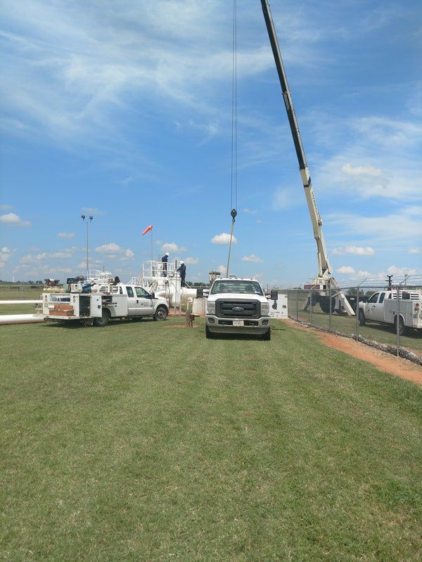 Several trucks are parked in a grassy field with a crane in the background