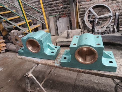 Dos cojinetes industriales de color verde azulado con casquillos de bronce reposan sobre una mesa de madera en un taller mecánico.