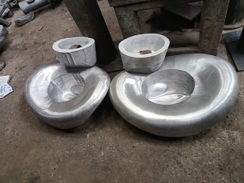 Dos piezas de metal fundido pulido, con forma de riñón y con cubetas centrales, reposan sobre el polvoriento suelo de un taller.