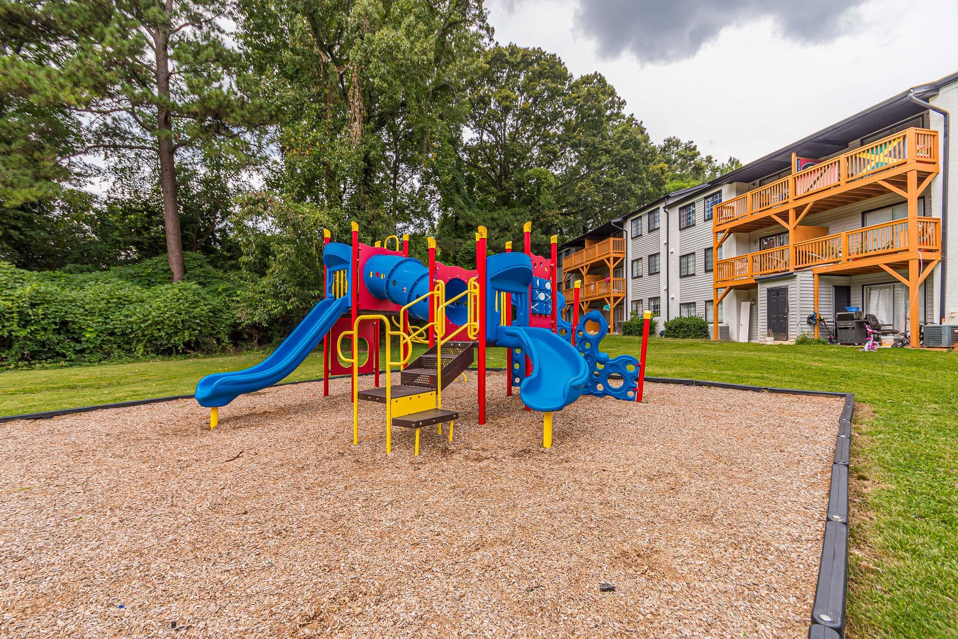 Colorful playground with slides and climbing bars on a woodchip surface beside apartment buildings
