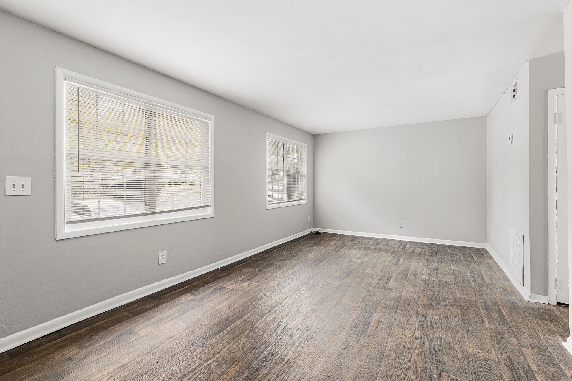 Empty room with gray walls, wood flooring, and two windows letting in daylight.