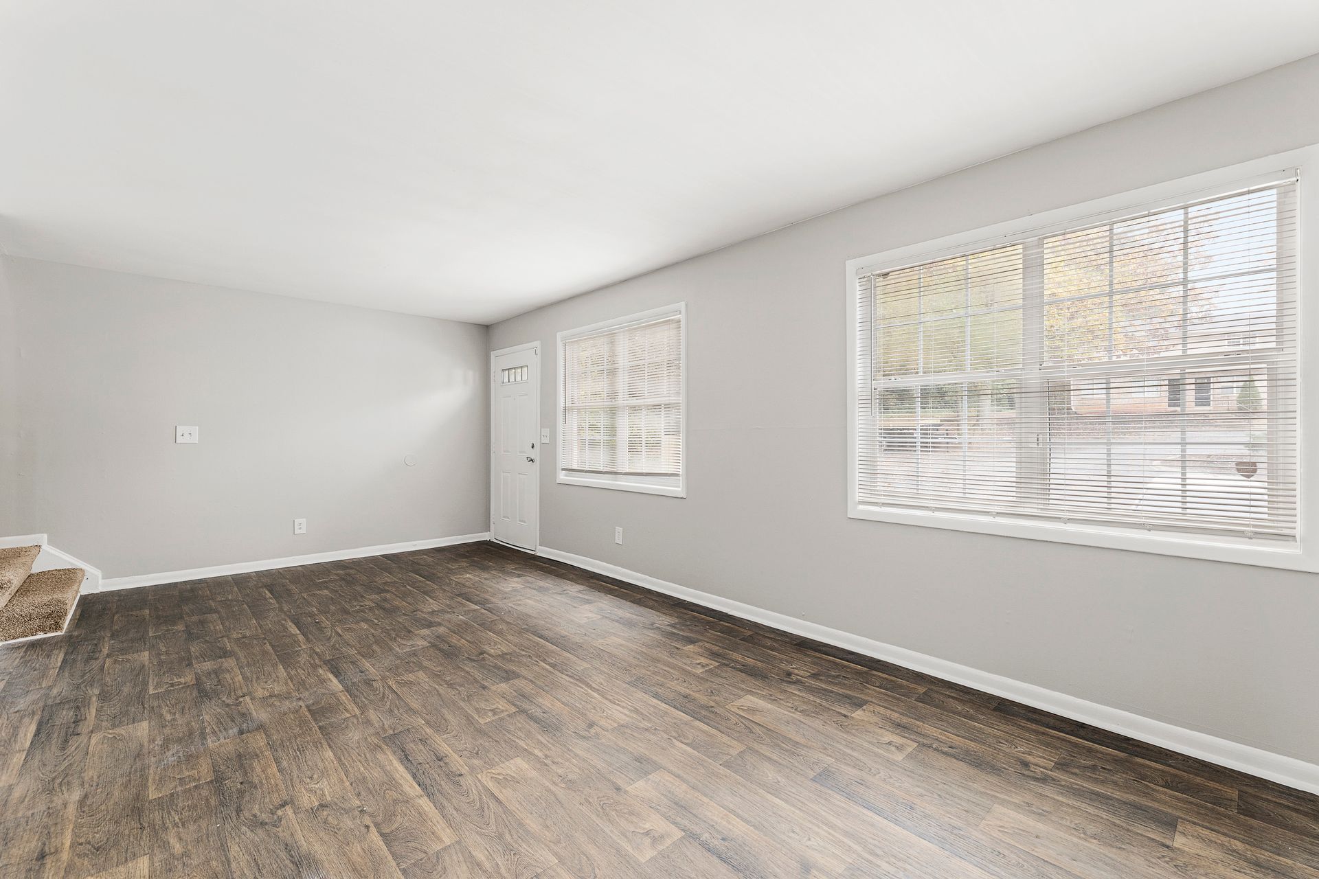 Empty bright room with gray walls, wood-look flooring, and two large windows.