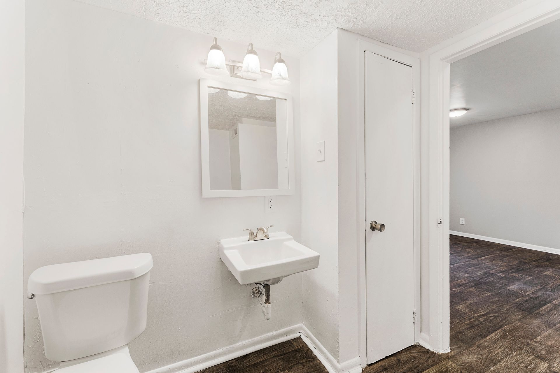 White bathroom with toilet, small sink, mirror, and open doorway to hall