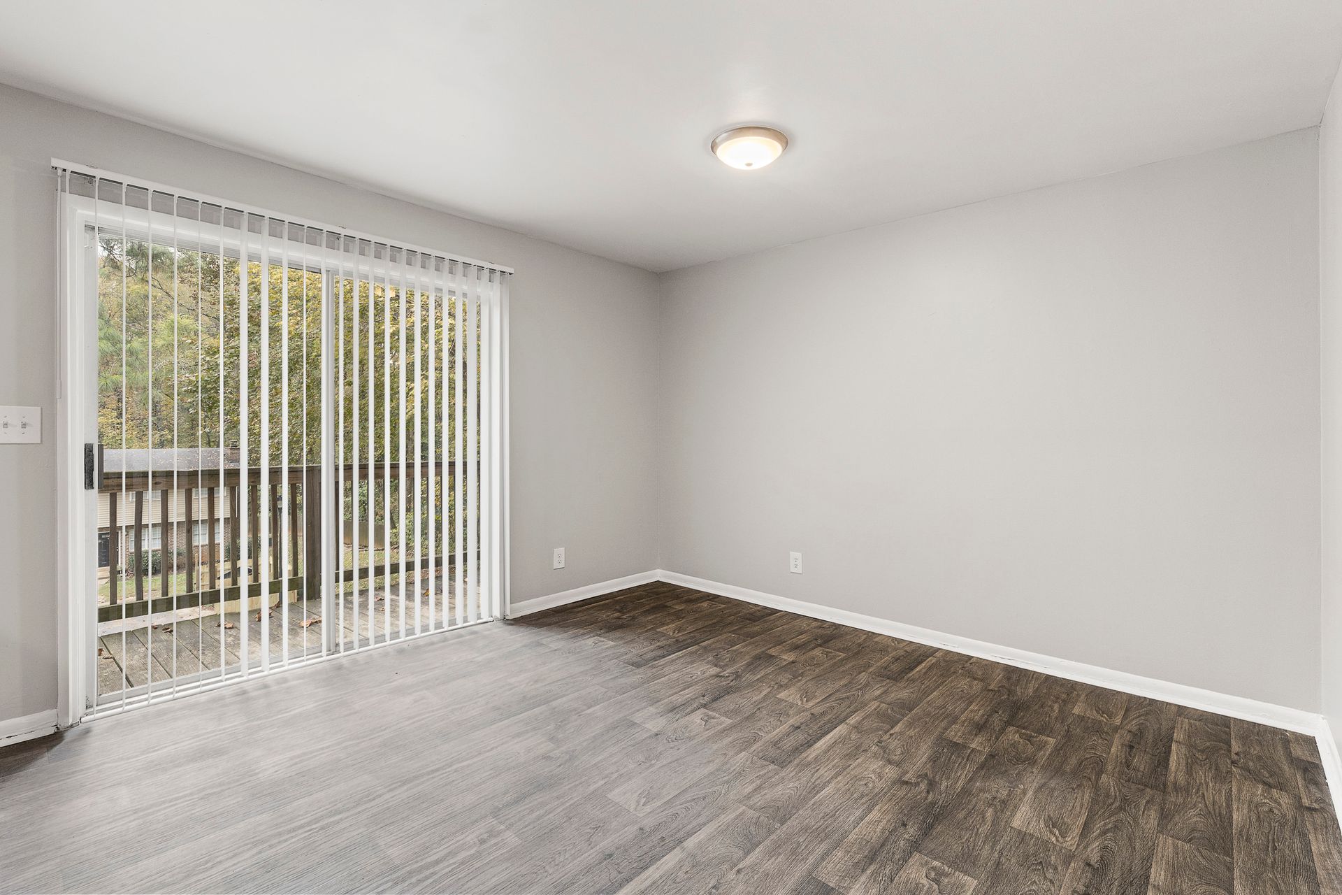 Empty room with gray wood flooring, white walls, and sliding glass doors with vertical blinds