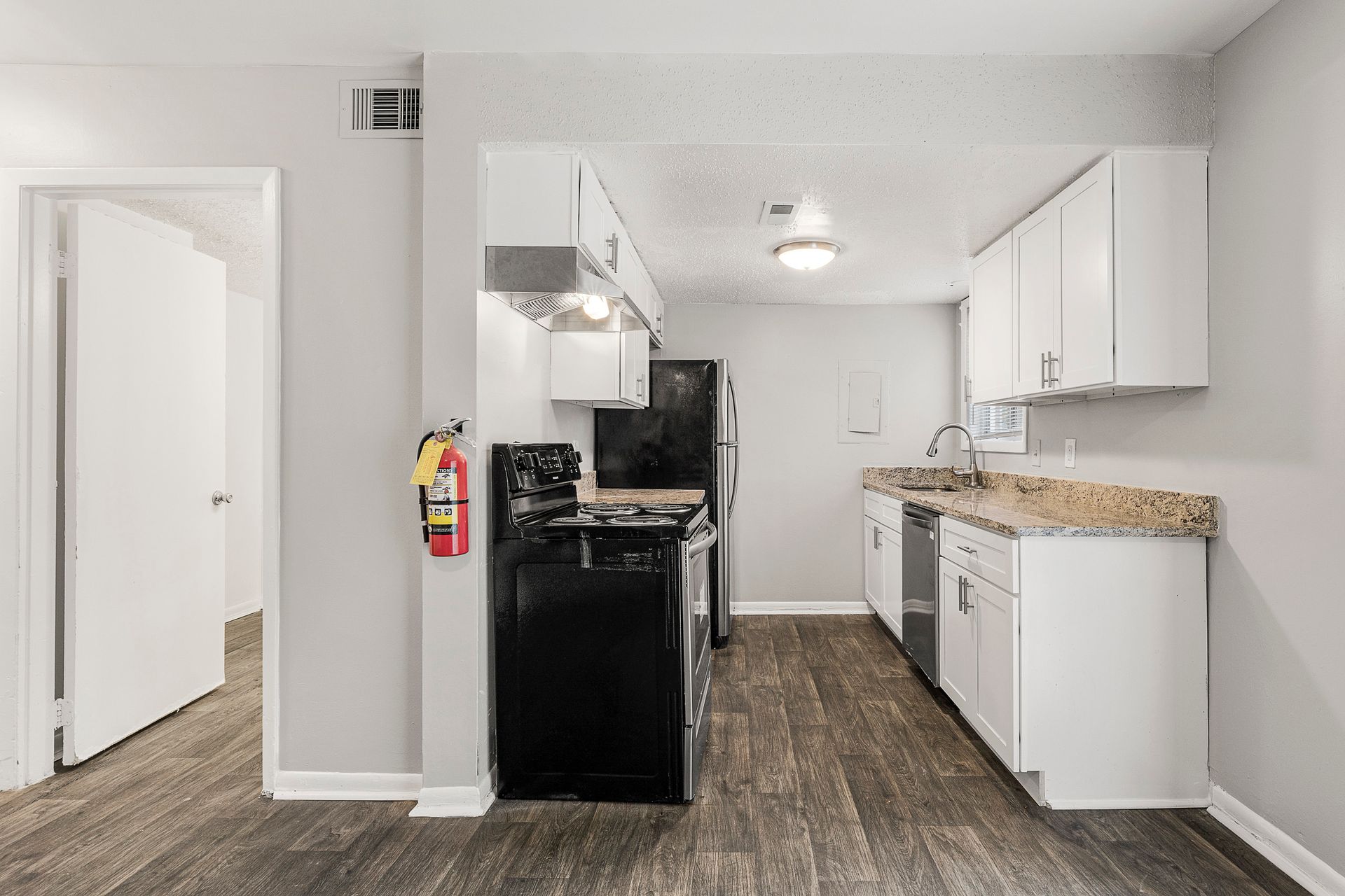 Small kitchen with white cabinets, black stove, granite counters, and wood-look flooring, viewed from the entryway