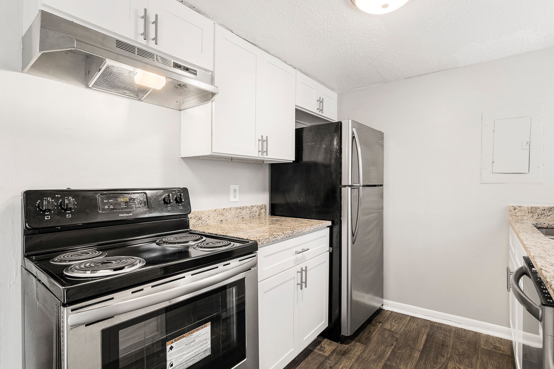 Bright modern kitchen with black stove, white cabinets, stainless fridge, and granite counters.