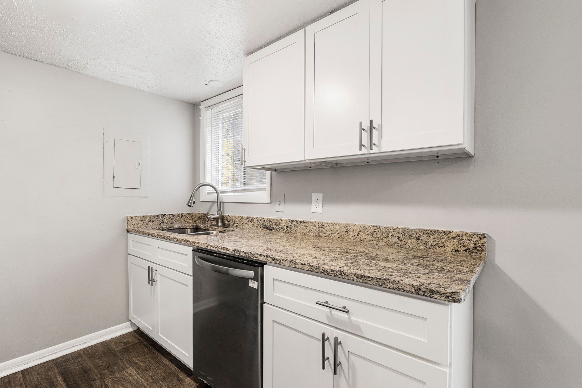 Small white kitchen with granite countertop, white cabinets, dishwasher, and window nook