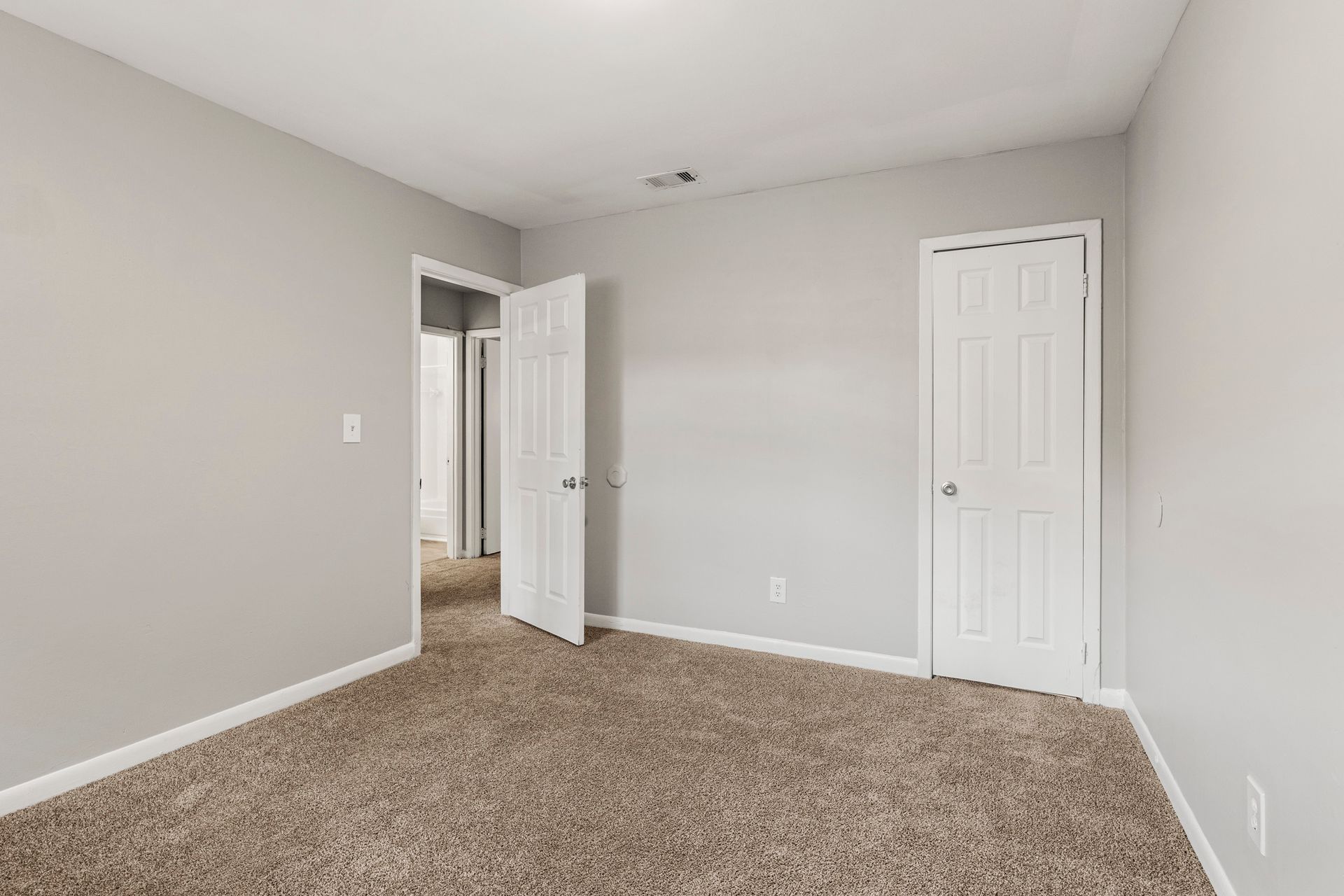 Empty beige-carpeted bedroom with light gray walls and two white doors.