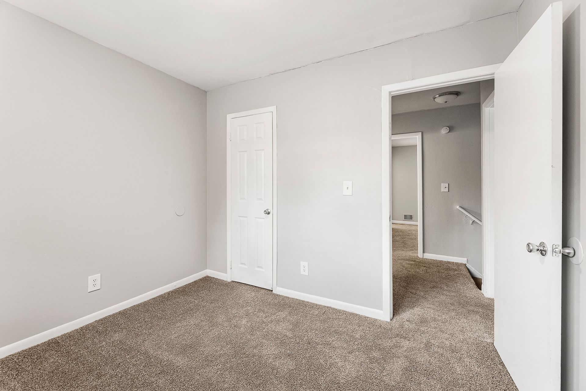 Empty gray carpeted bedroom with open white door and closet entrance