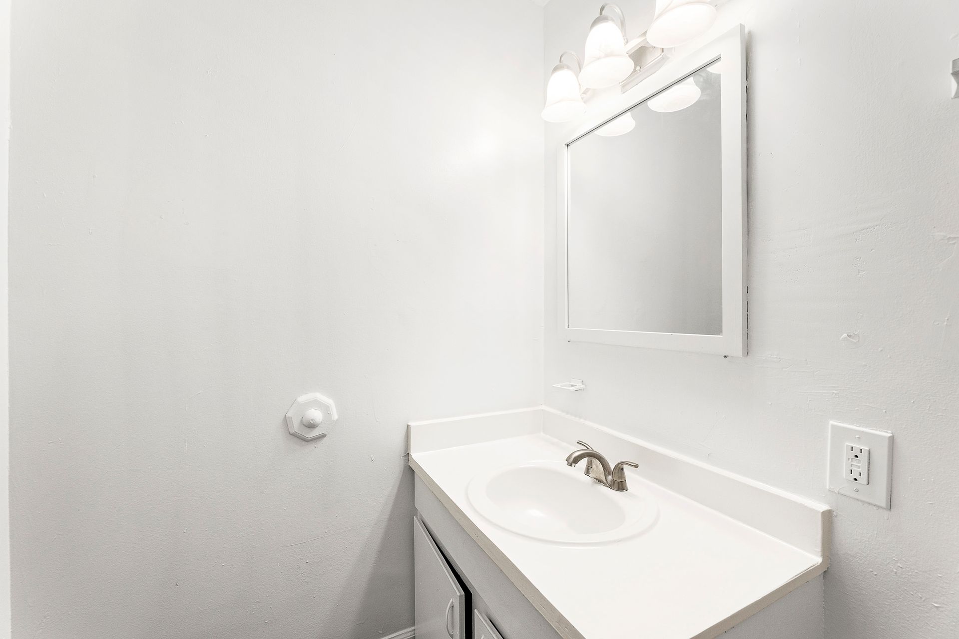 Bright bathroom vanity with white sink, mirror, and wall light above a light gray wall.