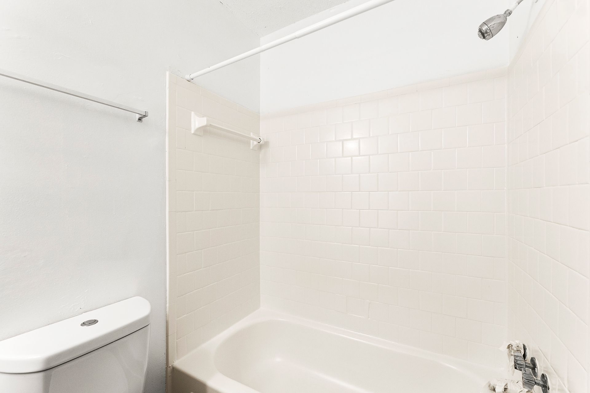 Bright white bathroom with a bathtub, shower curtain, toilet, and tiled walls.