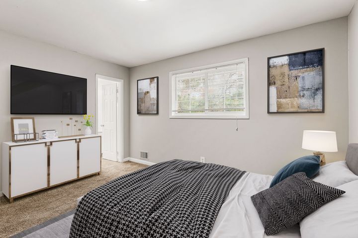 Modern bedroom with bed, wall-mounted TV, white cabinet, and framed art on gray walls
