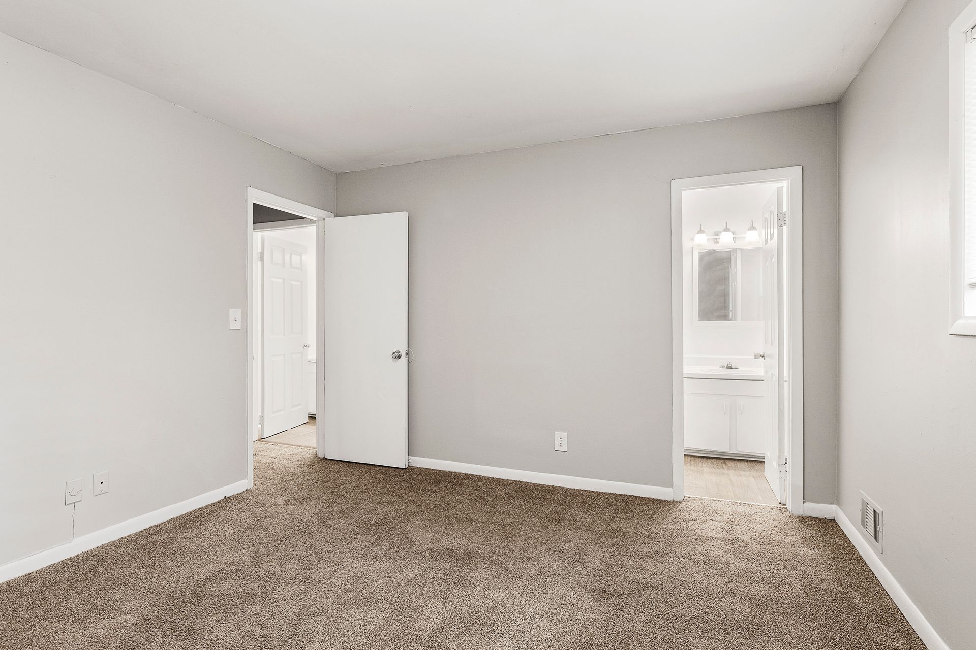 Empty carpeted bedroom with gray walls and an open door to a bathroom