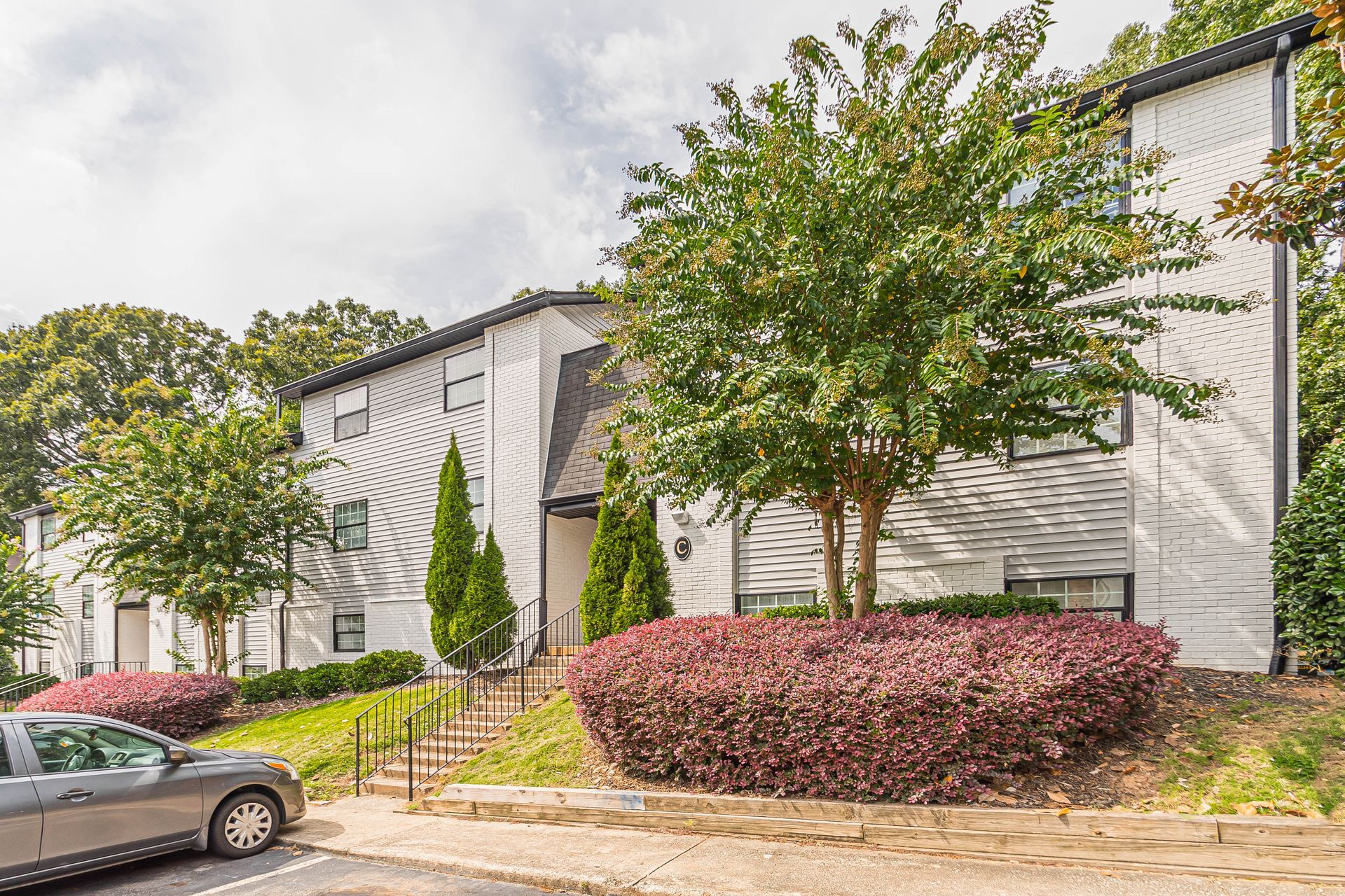Row of white apartment buildings with trees and parked cars on a cloudy day