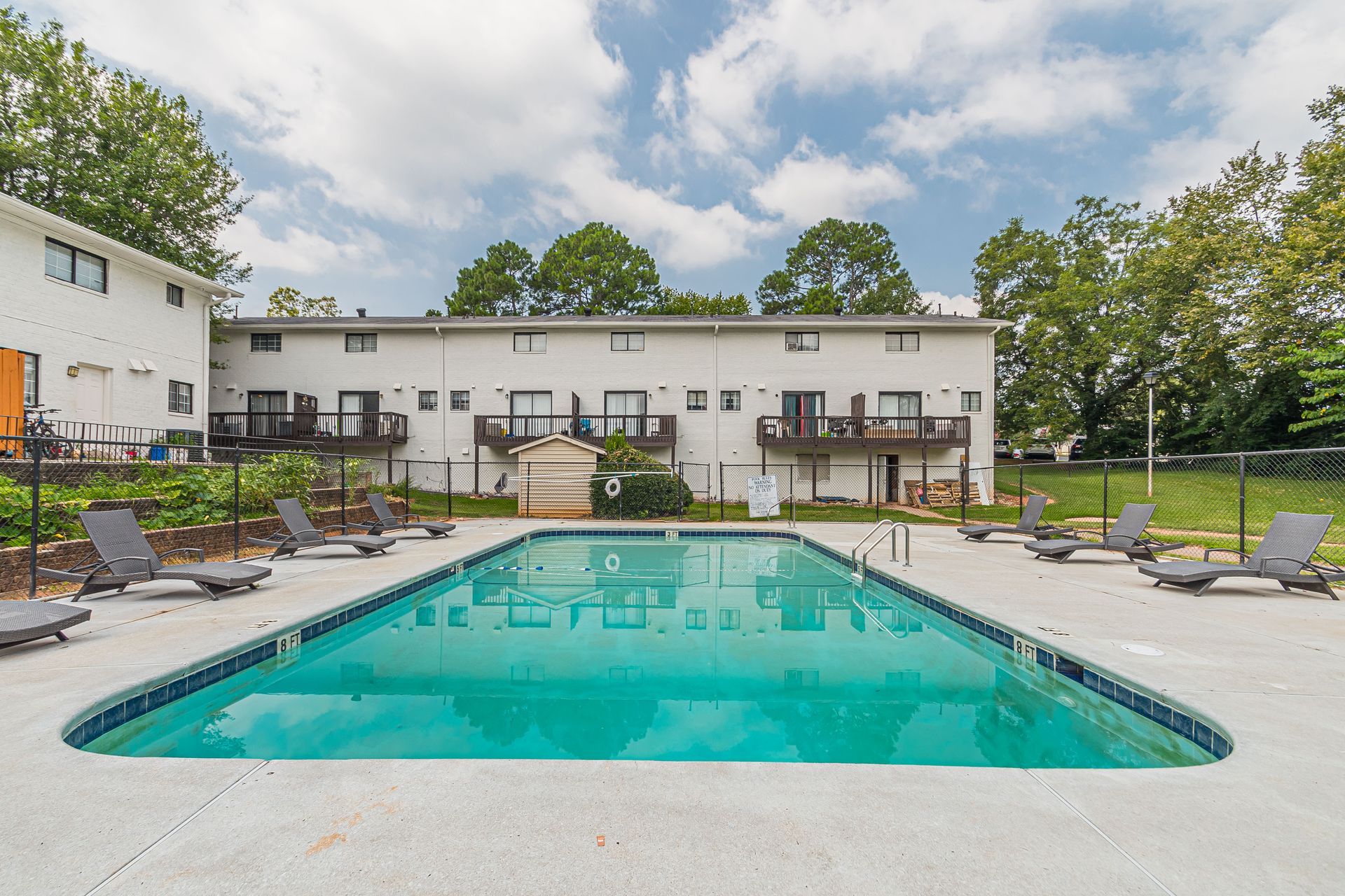 Apartment courtyard with turquoise swimming pool, lounge chairs, and a white building under a cloudy sky
