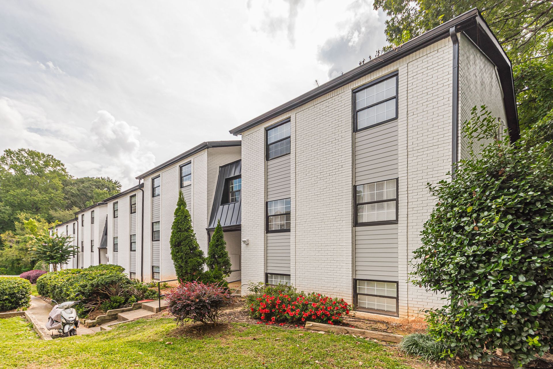 Apartment building with white siding, black-trim windows, and landscaped shrubs and flowers