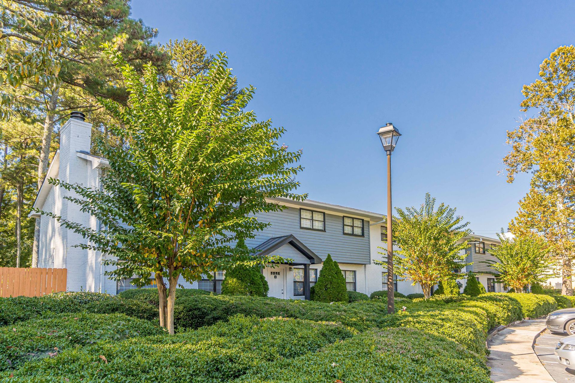 Tree-lined suburban house with green shrubs, a streetlamp, and a curved road under a clear blue sky