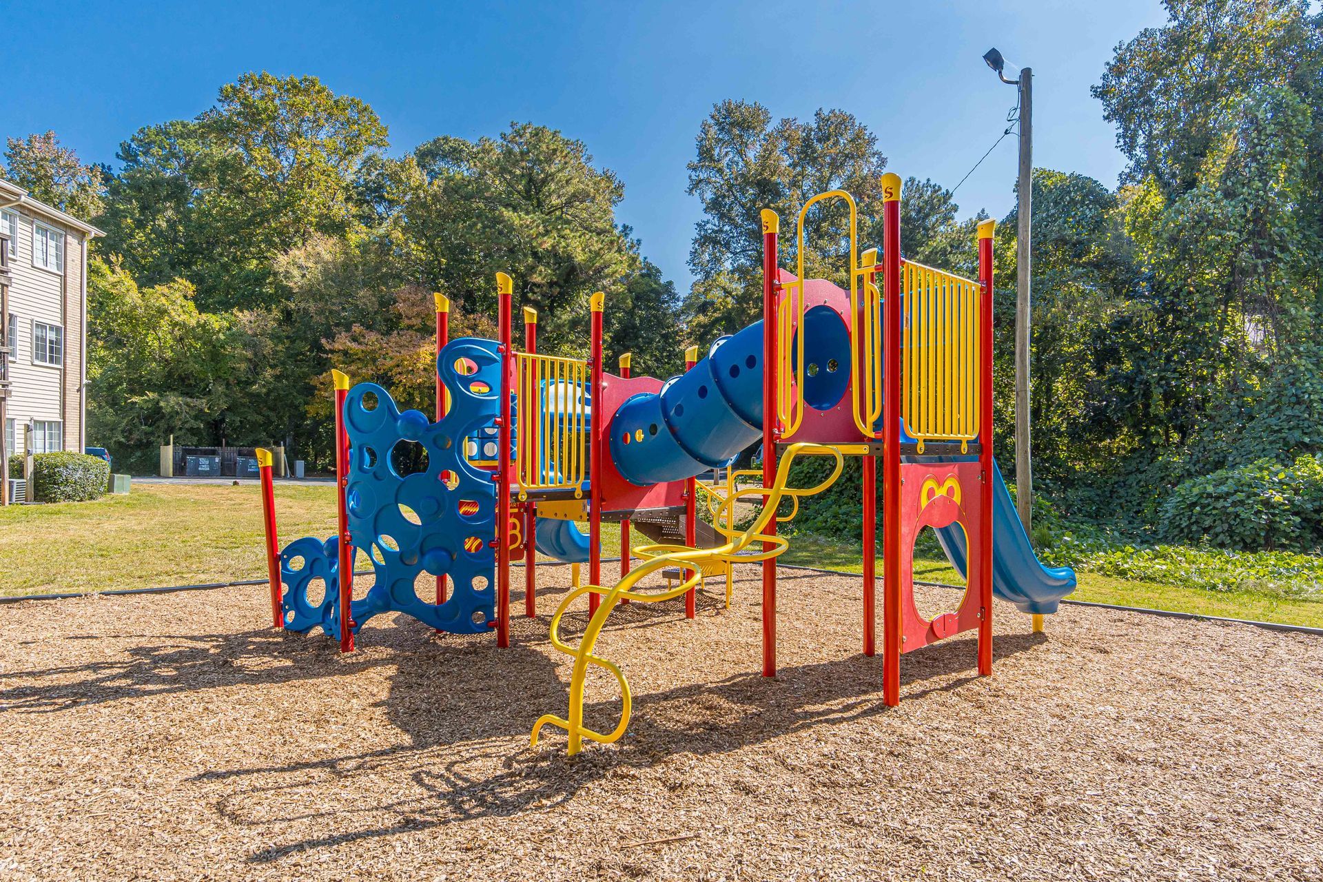 Colorful playground with slides, climbing walls, and red/yellow play structure on a woodchip surface outdoors.