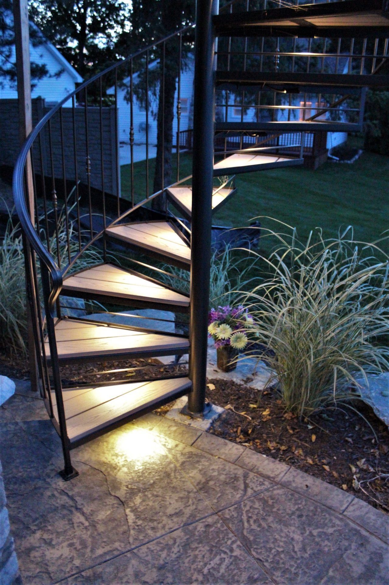 A spiral staircase is lit up at night in a backyard.