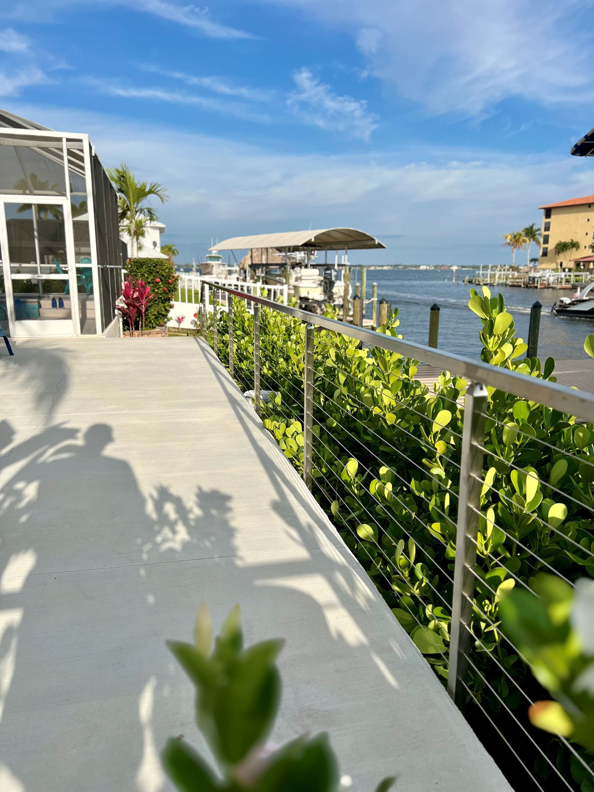 A shadow of a person is cast on a concrete walkway next to a body of water