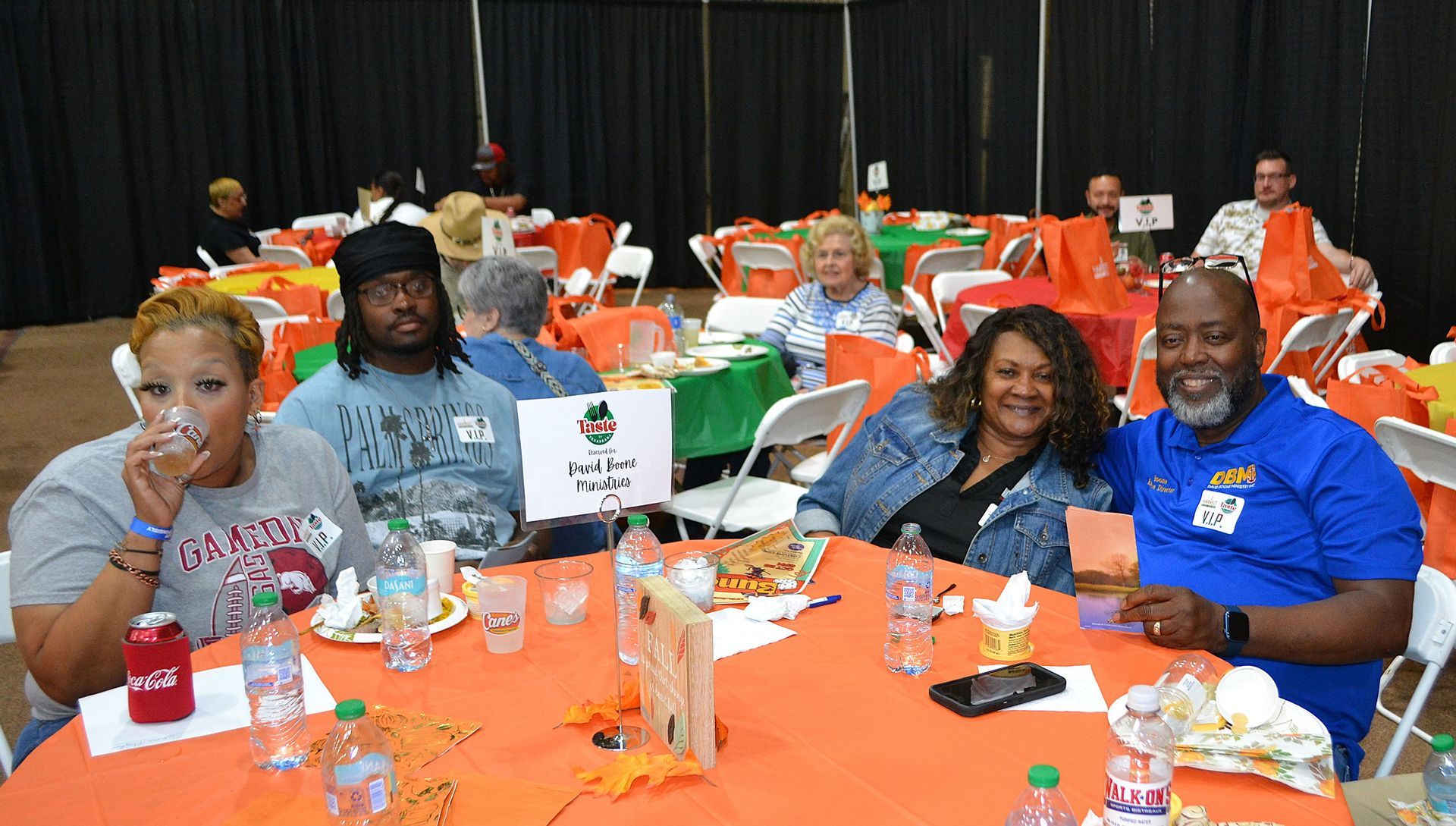 People seated at orange-clothed tables during a banquet, smiling and posing for a photo.