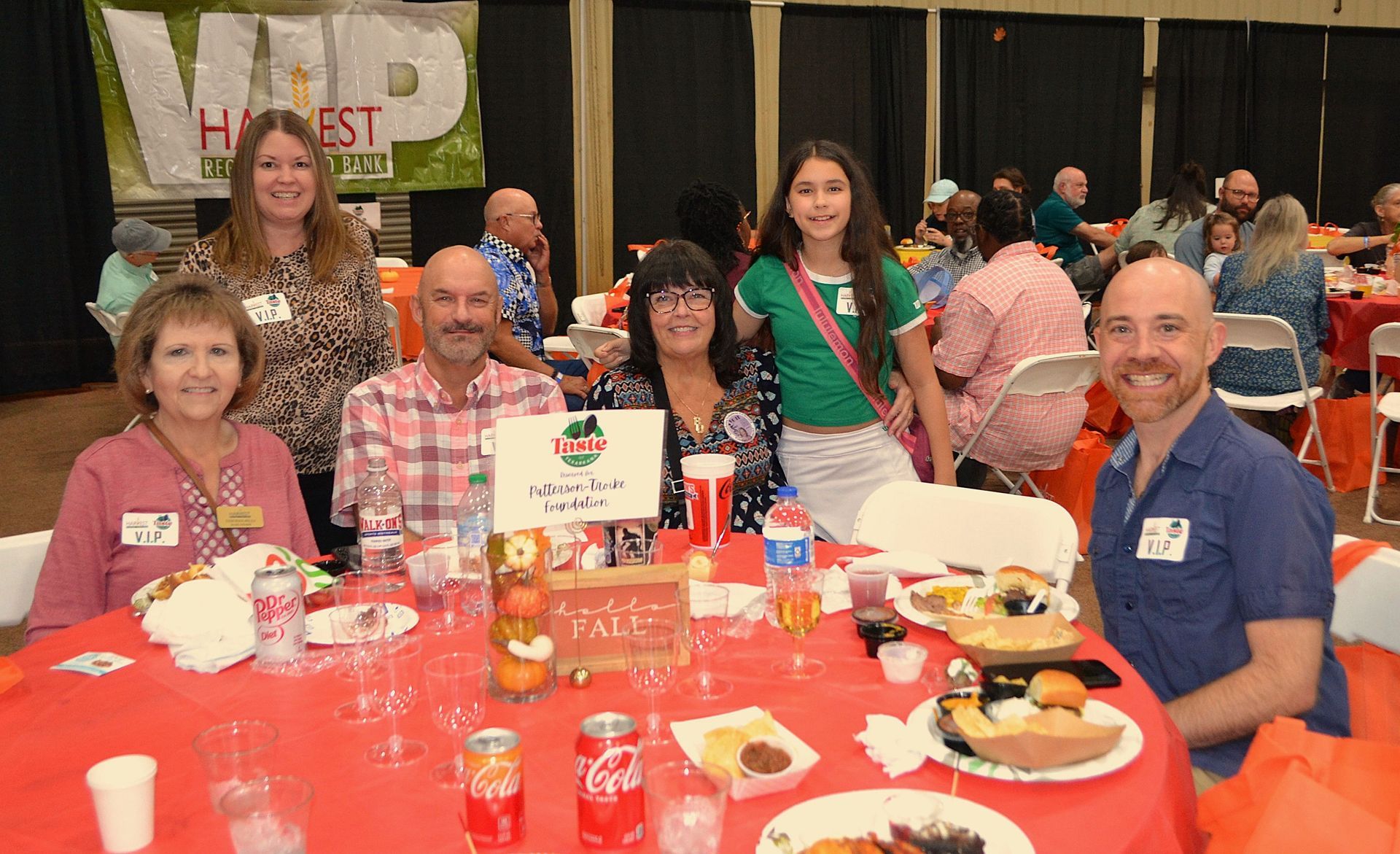 Group seated at a banquet table with food and drinks, posing in a lively event hall.