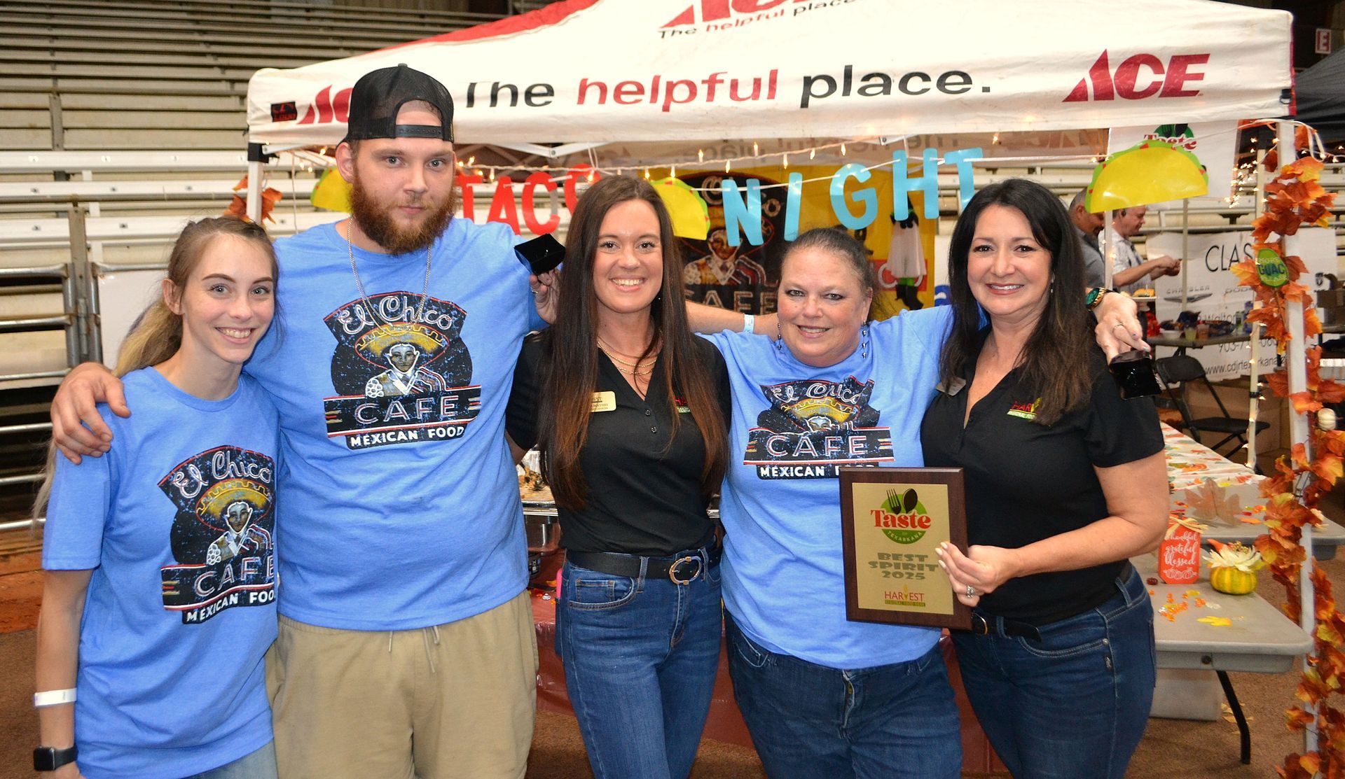 Five people in blue shirts posing at an ACE Hardware booth, one holding a plaque.