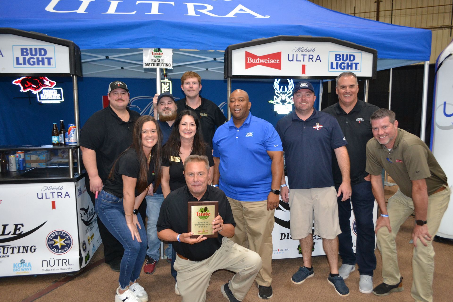 Group posing at an Ultra Bud Light tent, with one man kneeling holding a plaque.