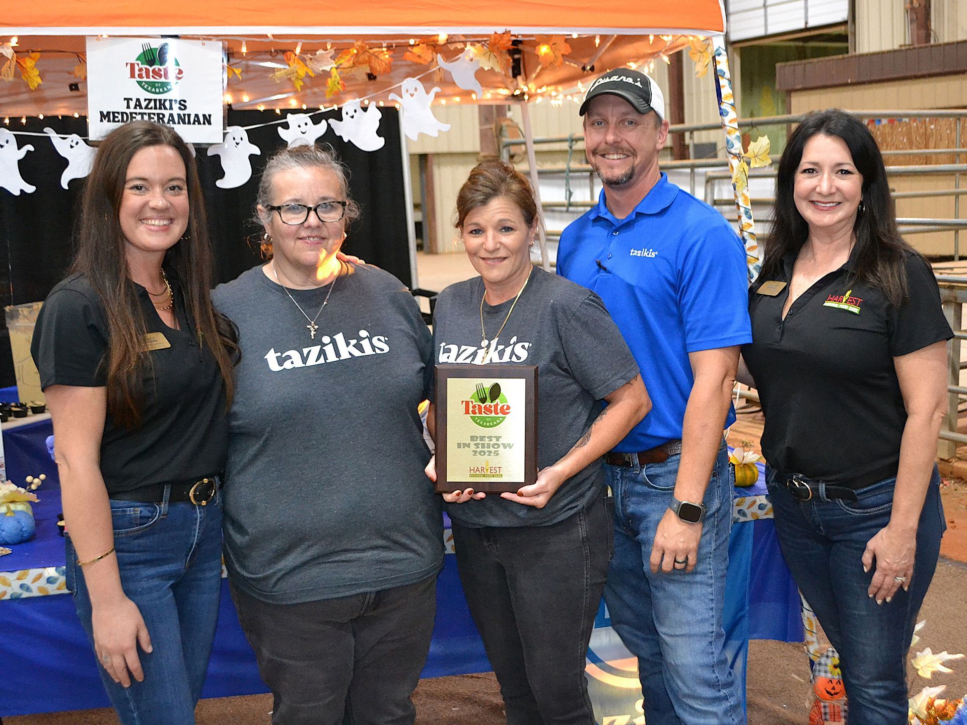 Five people standing at a booth, holding a framed award plaque and smiling indoors