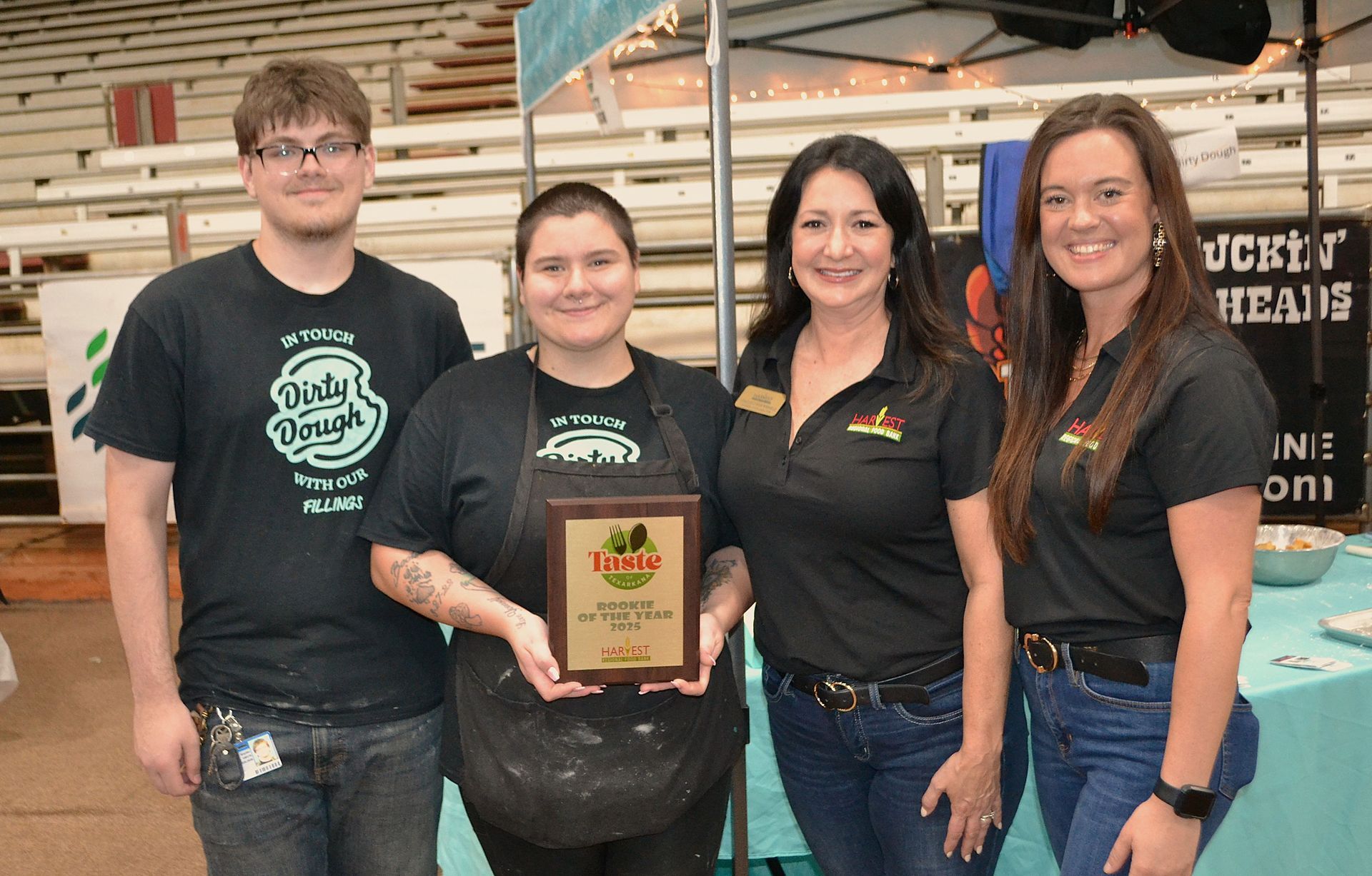 Four people posing indoors, holding a plaque in a rustic event space.