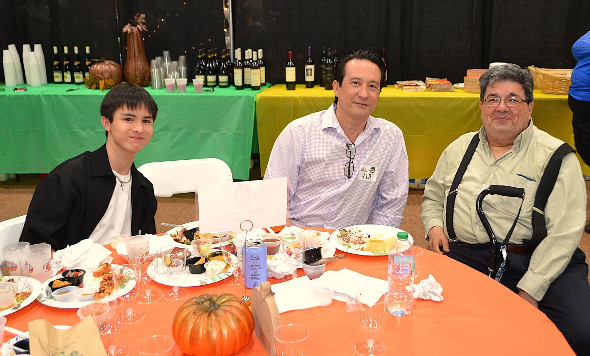 Three people seated at a banquet table with food and a pumpkin centerpiece in a decorated hall