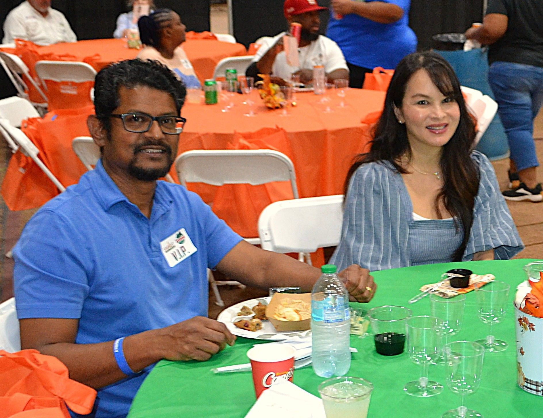 Two people seated at a banquet table with green tablecloths in an event hall