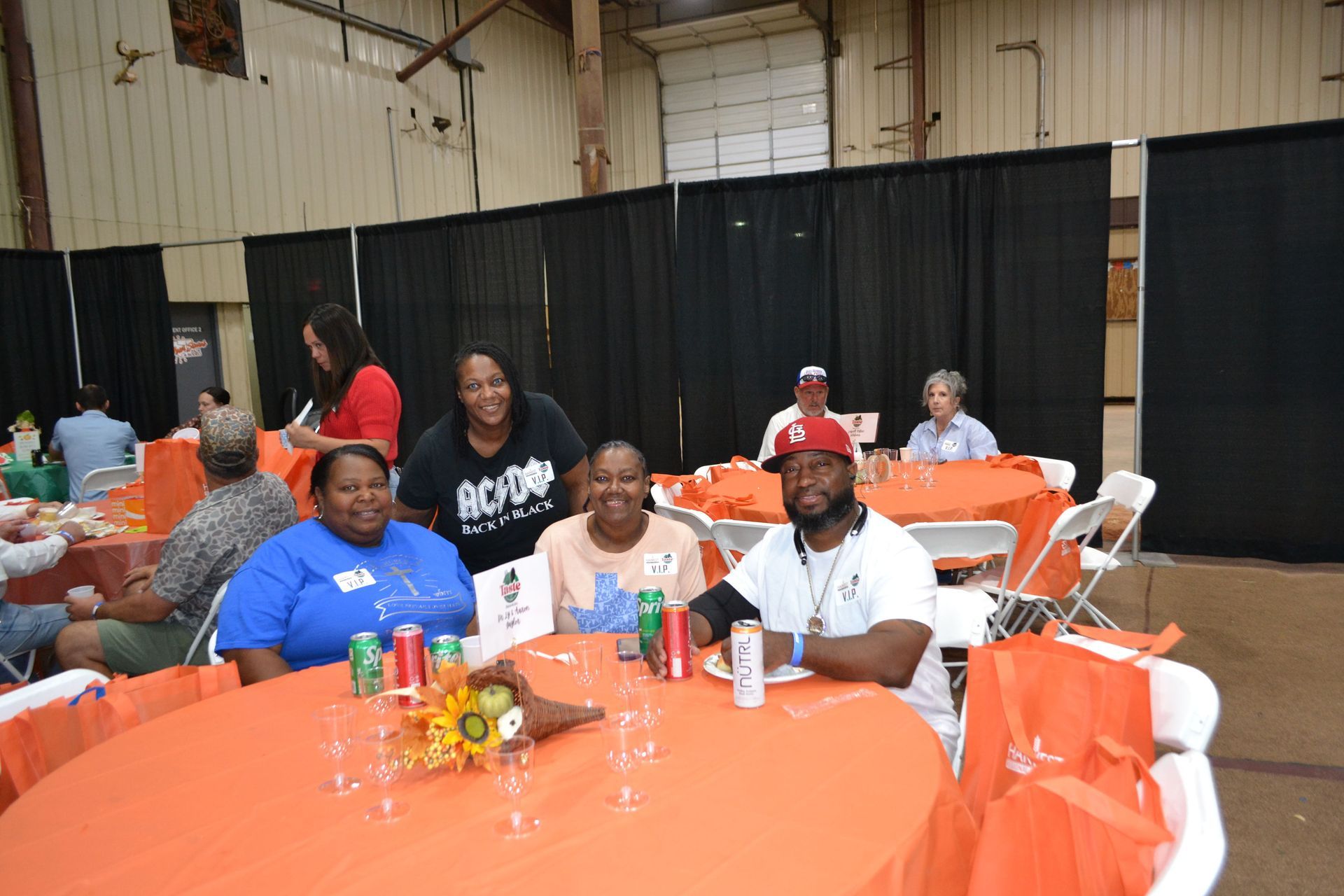 People seated at orange round tables in a banquet hall with black curtains and white walls