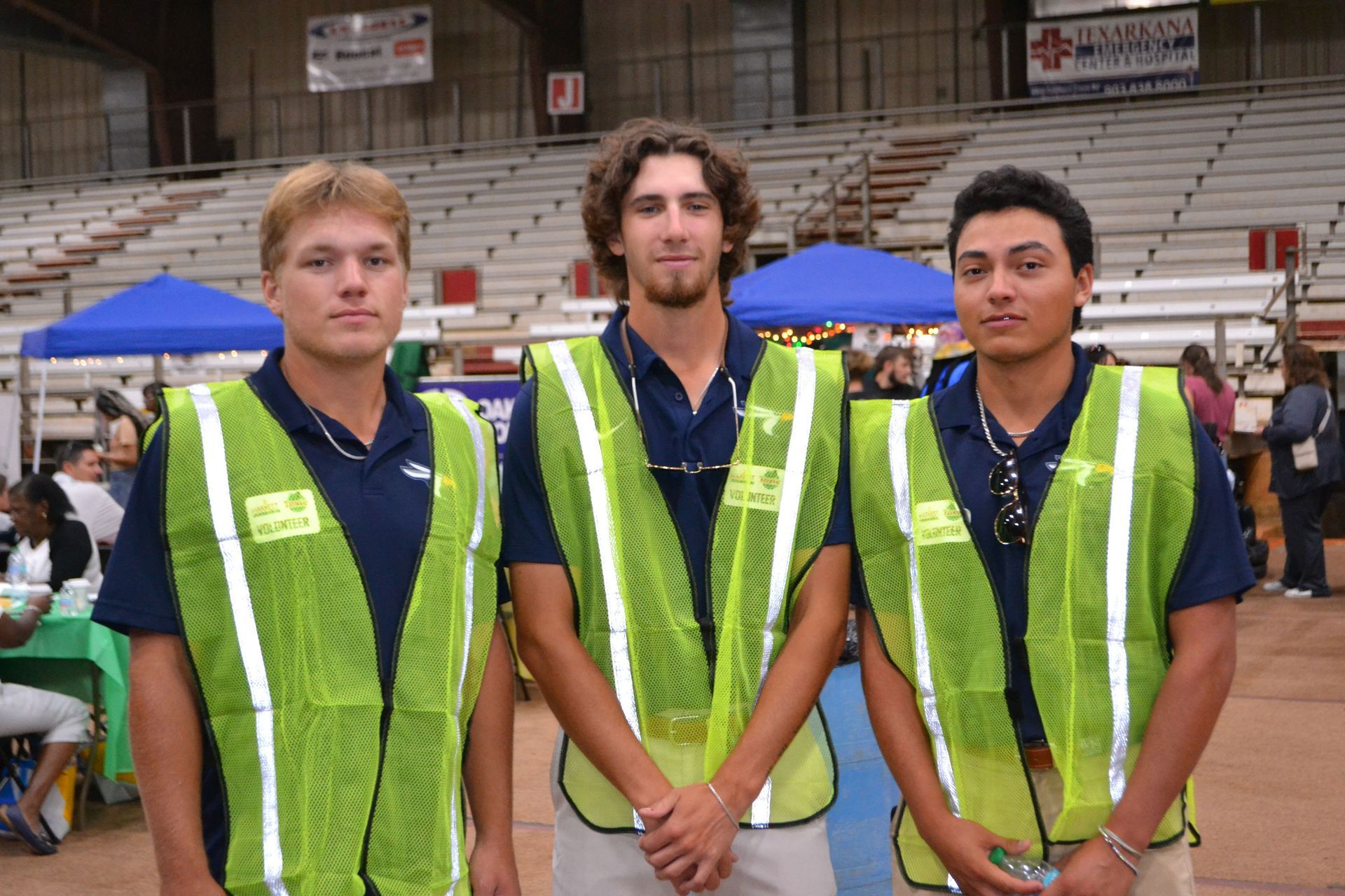 Three volunteers in lime-green safety vests standing indoors at an event venue