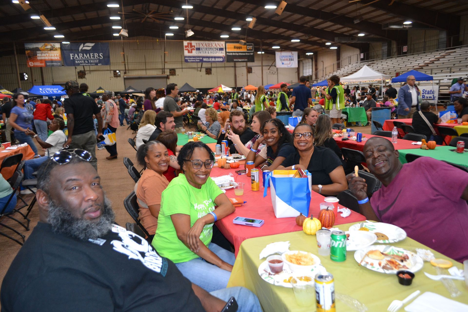 Crowded indoor banquet with people seated at long tables, smiling and eating under a large hall ceiling.