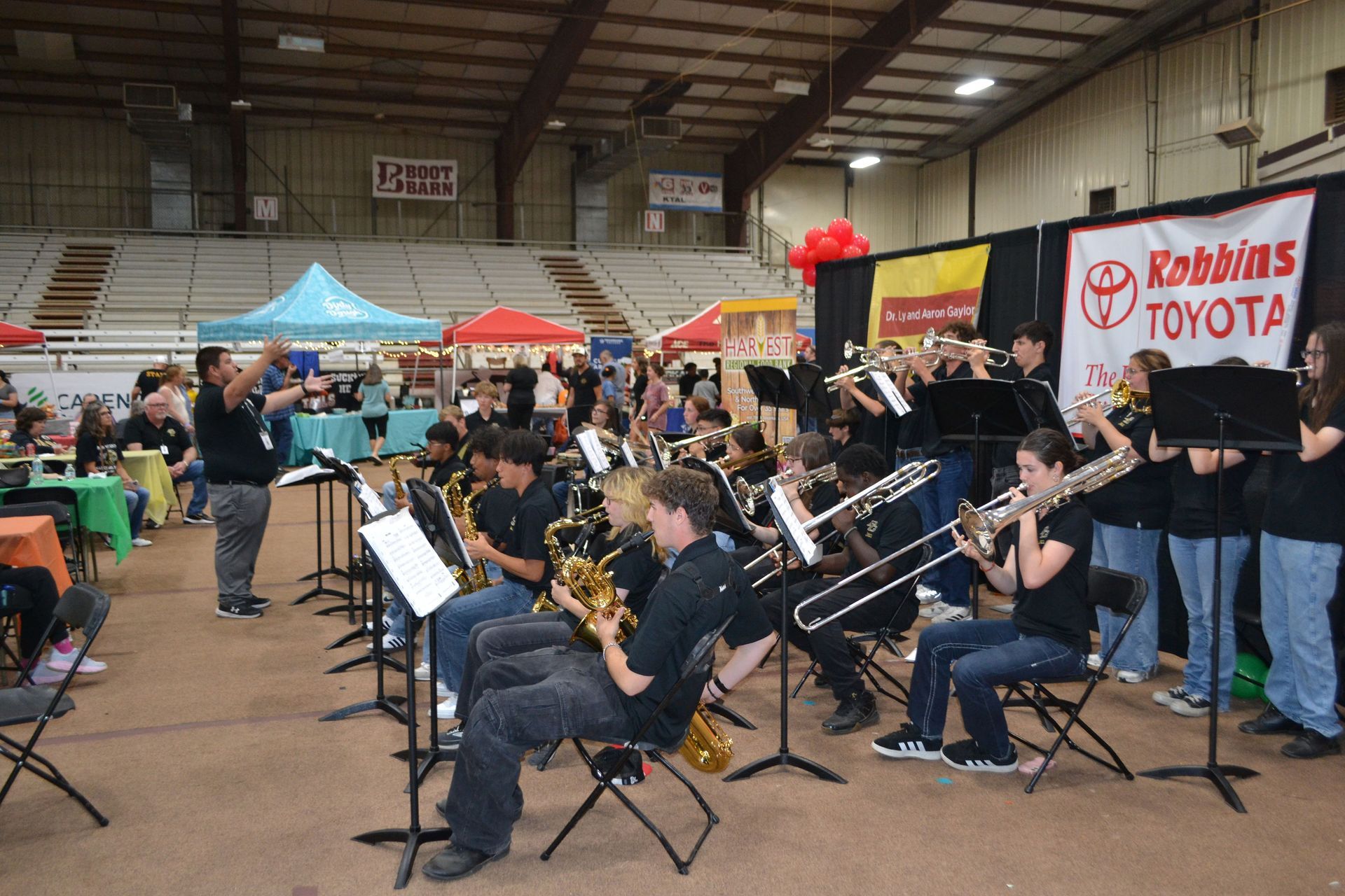 Band orchestra playing indoors at a festival booth area, with people watching in the background.