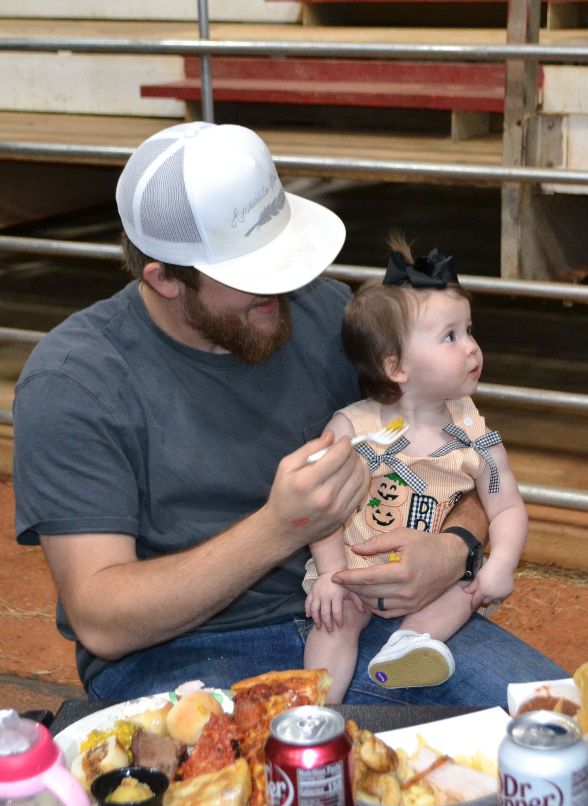 Man feeding a toddler at a table with food and drinks in a casual indoor setting