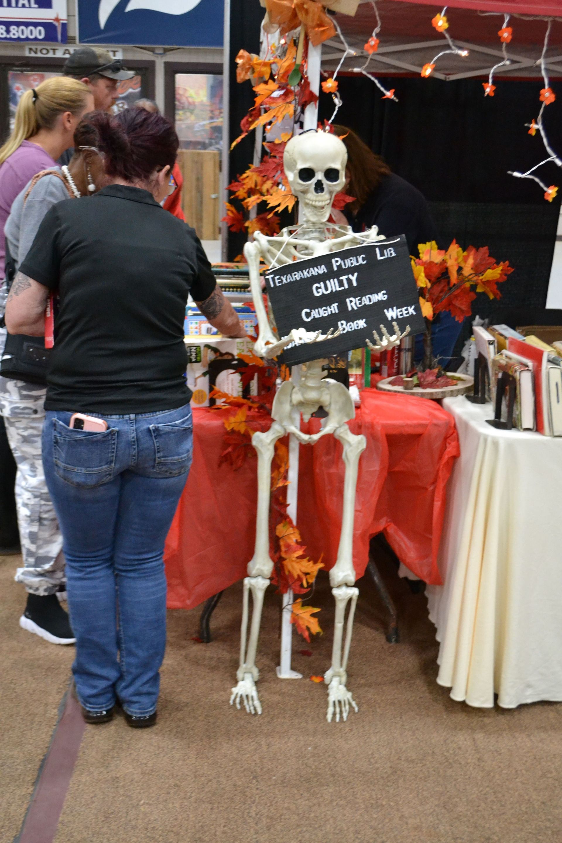 Skeleton Halloween display at a booth, with orange decorations and a chalkboard sign beside it