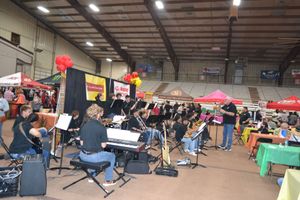 Live band performing in an indoor fair hall, with tents, tables, and balloons in the background.